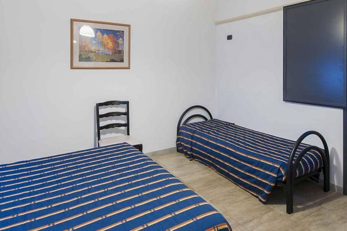 Una habitación con dos camas, una silla, un cuadro y un televisor.