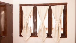 A room with a wooden wardrobe and a window with three curtains tied back. - Donna Alda Casa (Salta)