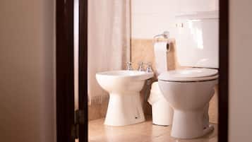 A bathroom with a toilet, bidet, and a roll of toilet paper on the wall.