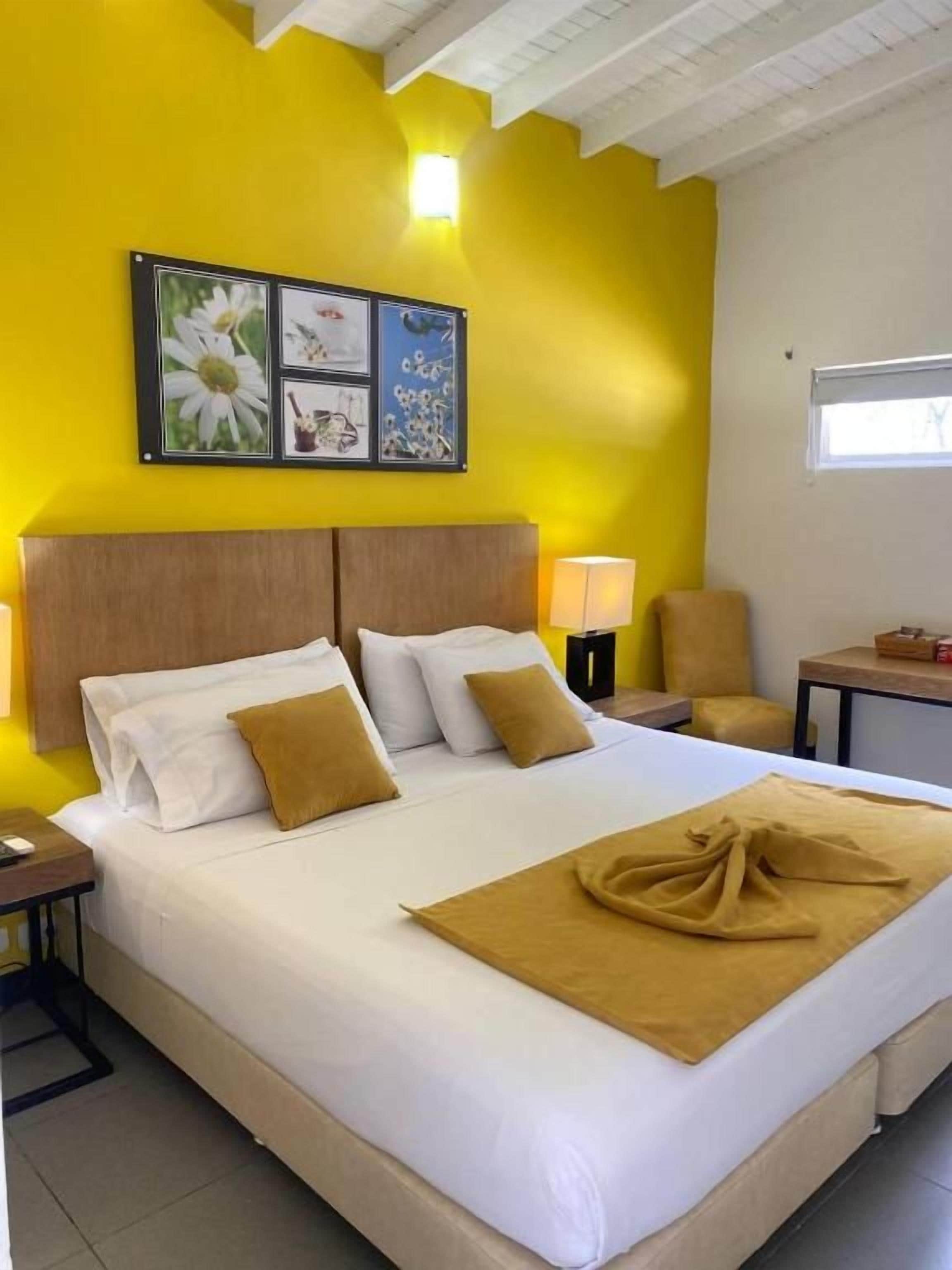 Habitación de hotel con una cama grande, cabecera, mesita de noche, silla, mesa y ventana.