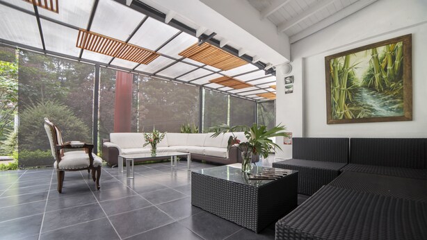 A modern indoor space with a white sofa, a wooden chair, and a black woven sofa. There are potted plants and a painting on the wall. - Hotel Aromax del Campestre (Medellín)