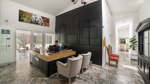 A reception desk with a receptionist, a large painting above, and a stone-tiled floor. - Hotel Aromax del Campestre (Medellín)