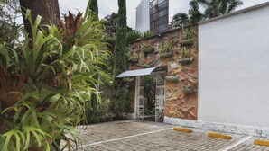 A paved entrance with a metal gate, a stone wall with plants, and a white building in the background. - Hotel Aromax del Campestre (Medellín)
