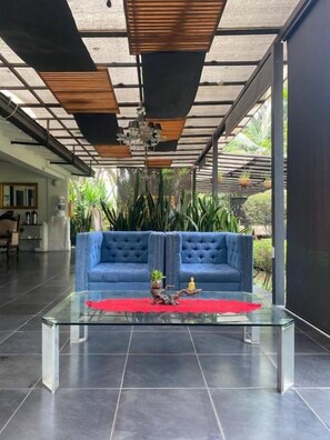 A modern living room with a glass coffee table, a blue sofa, and a ceiling with wooden slats. - Hotel Aromax del Campestre (Medellín)