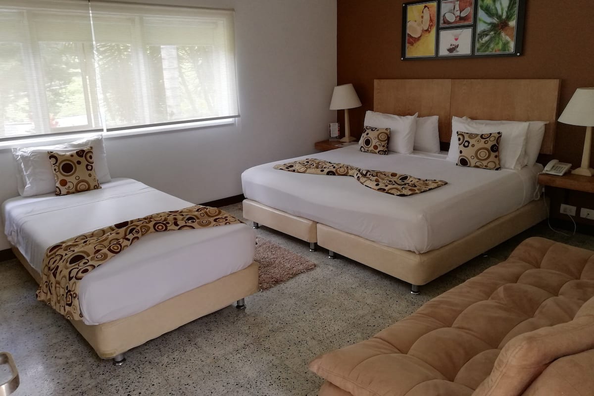 Ein Hotelzimmer mit zwei Betten, einem Sofa, einem großen Fenster, einem Wandbild und einem Telefon auf dem Nachttisch.