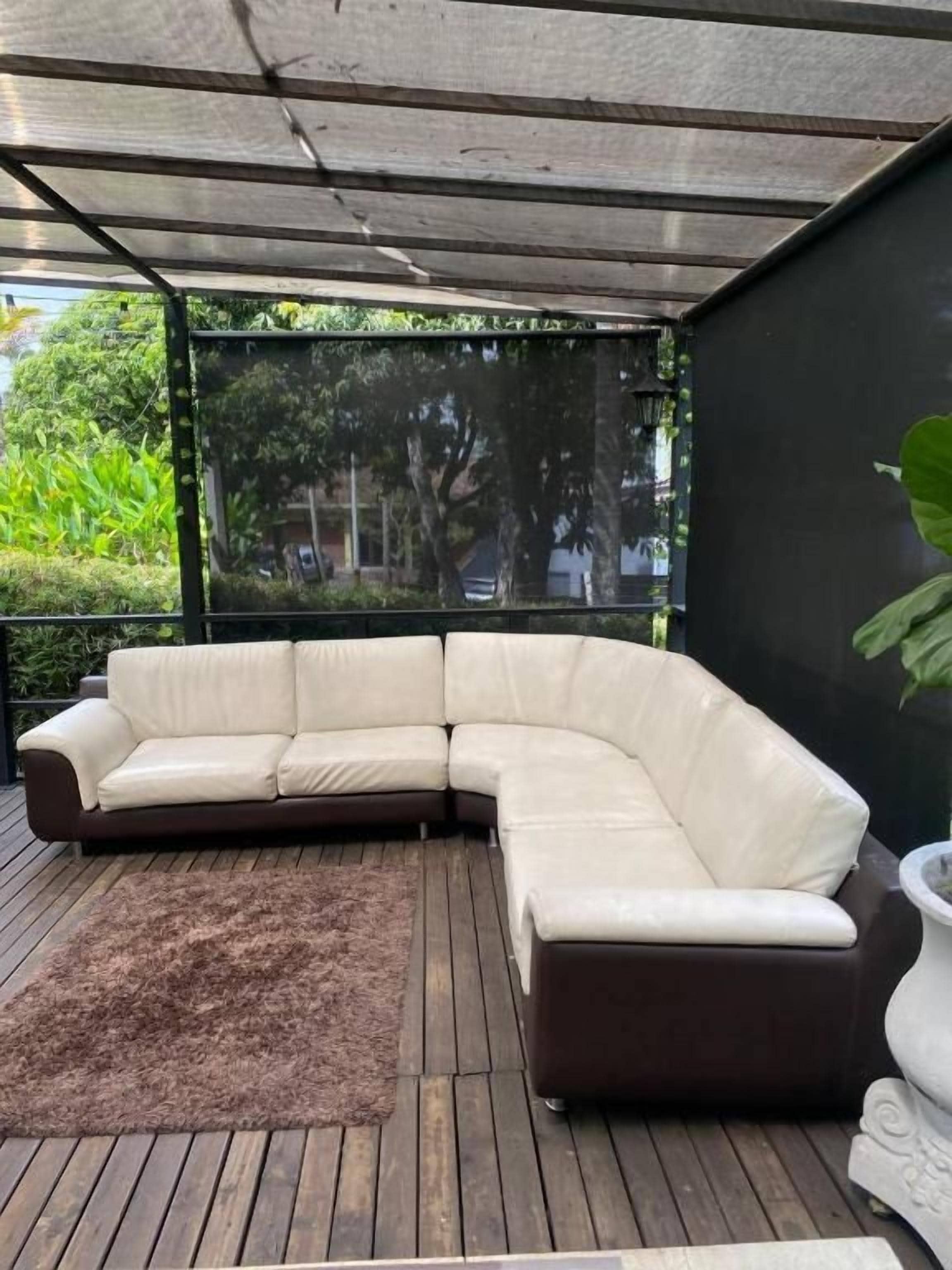 Un sofá modular sobre una terraza de madera, con vista a zonas verdes y un edificio al fondo.