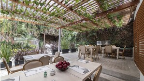 An outdoor dining area with tables and chairs, surrounded by lush greenery and a pergola structure. - Hotel Aromax del Campestre (Medellín)