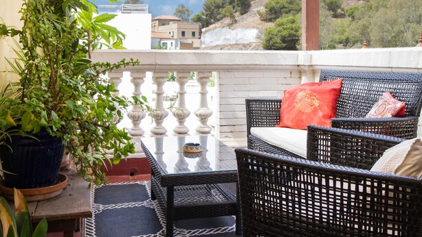 A balcony with wicker furniture, a glass table, and a potted plant. - Villa Alicia Guest House (Málaga)