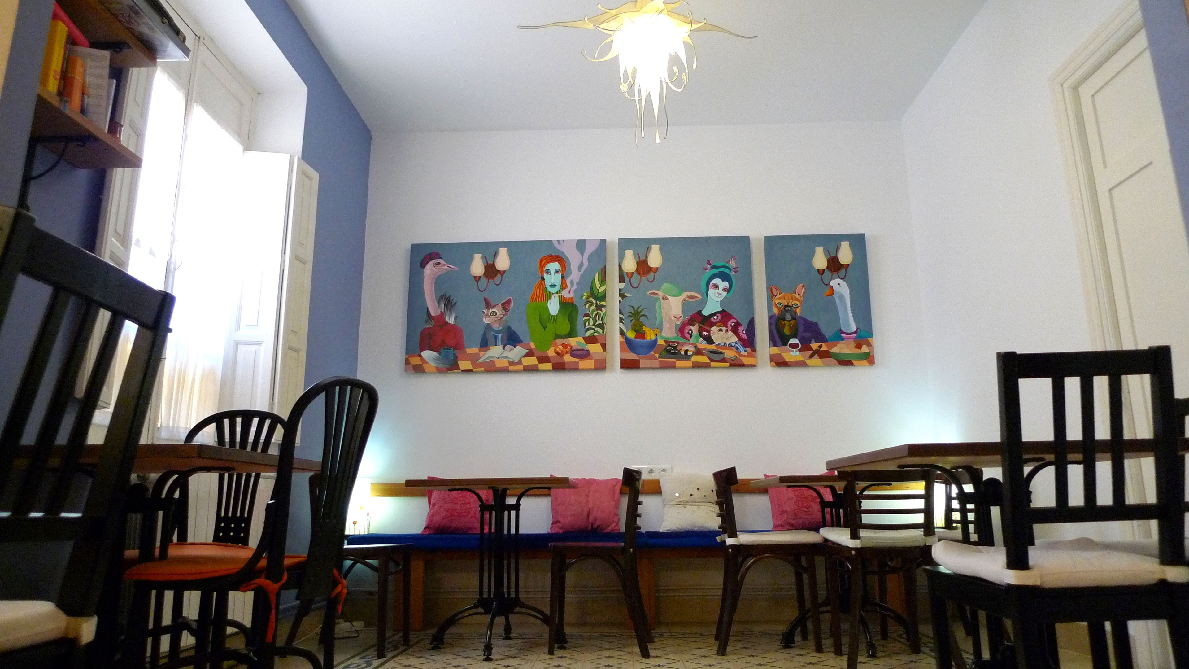 Uma sala de jantar com uma mesa posta para quatro pessoas, rodeada por cadeiras, e três quadros coloridos na parede.