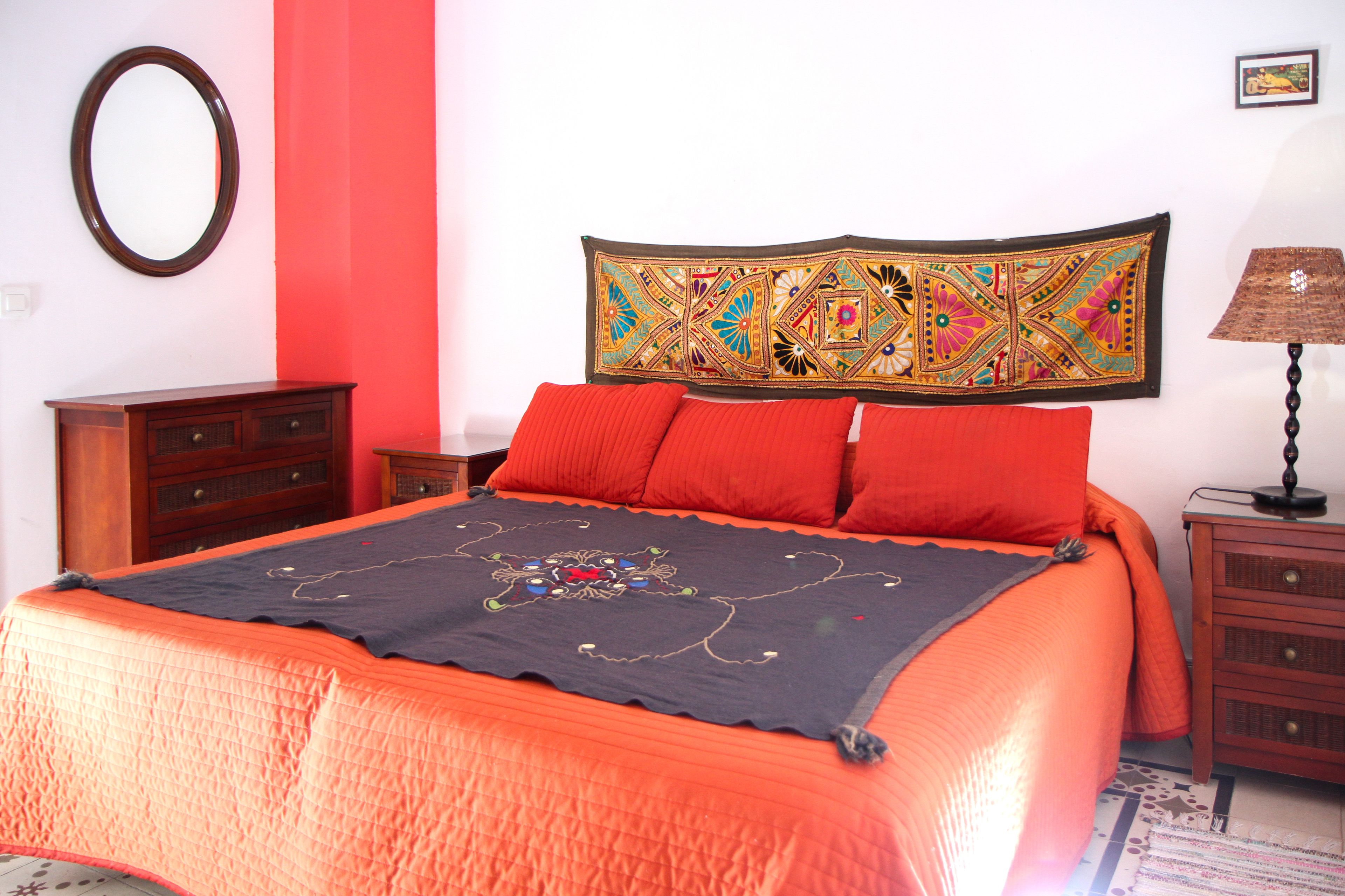 Un lit avec une tête de lit à motifs, des oreillers rouges et une couverture foncée.