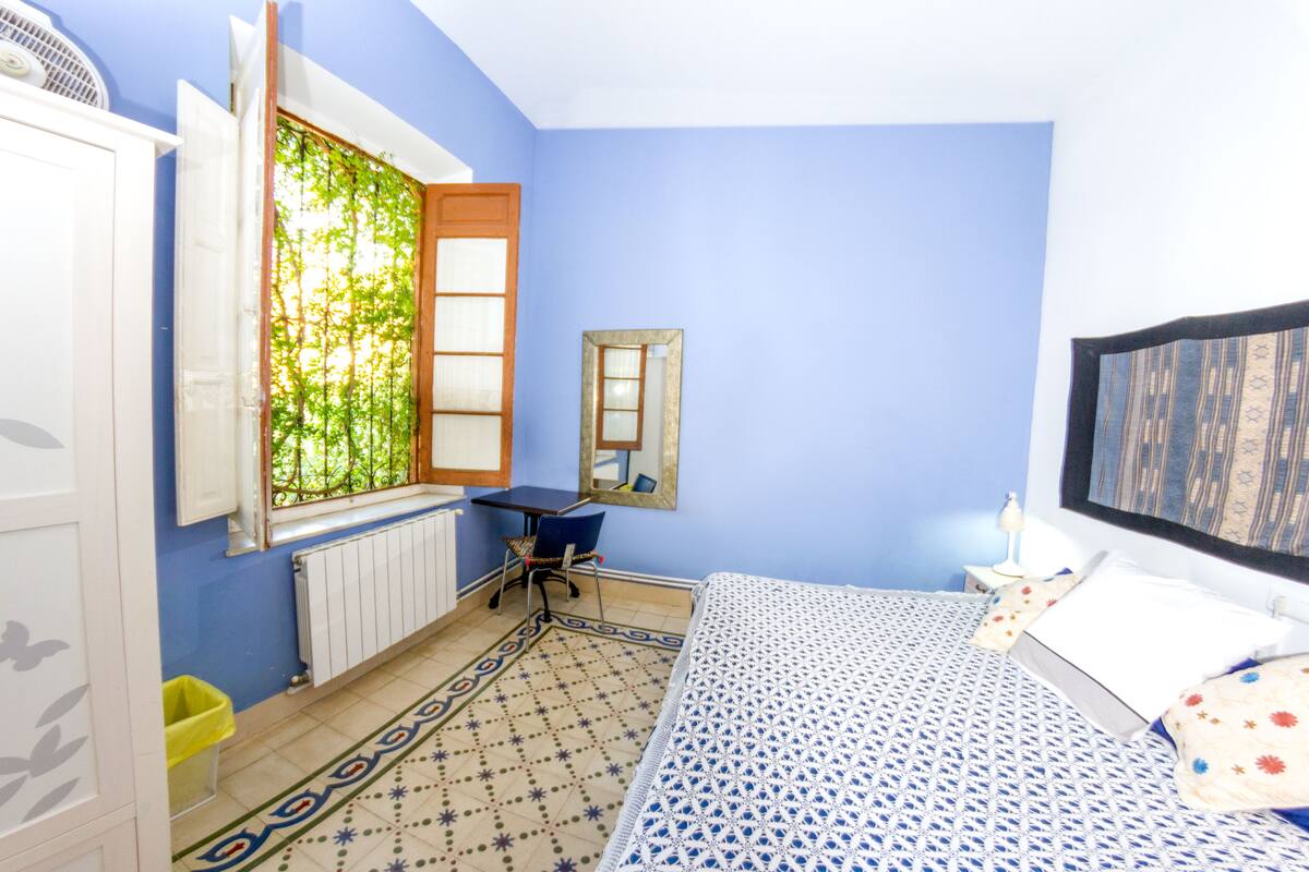 Une chambre à coucher avec un lit, une chaise, un radiateur, une fenêtre donnant sur un beau paysage et un miroir au mur.