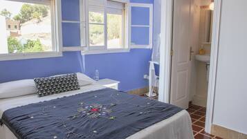A bedroom with a bed, a window, a bedside table, and a bathroom visible through an open door.