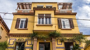 A two-story building with a yellow facade, a stone base, and a balcony with a wooden railing. - Villa Alicia Guest House (Málaga)
