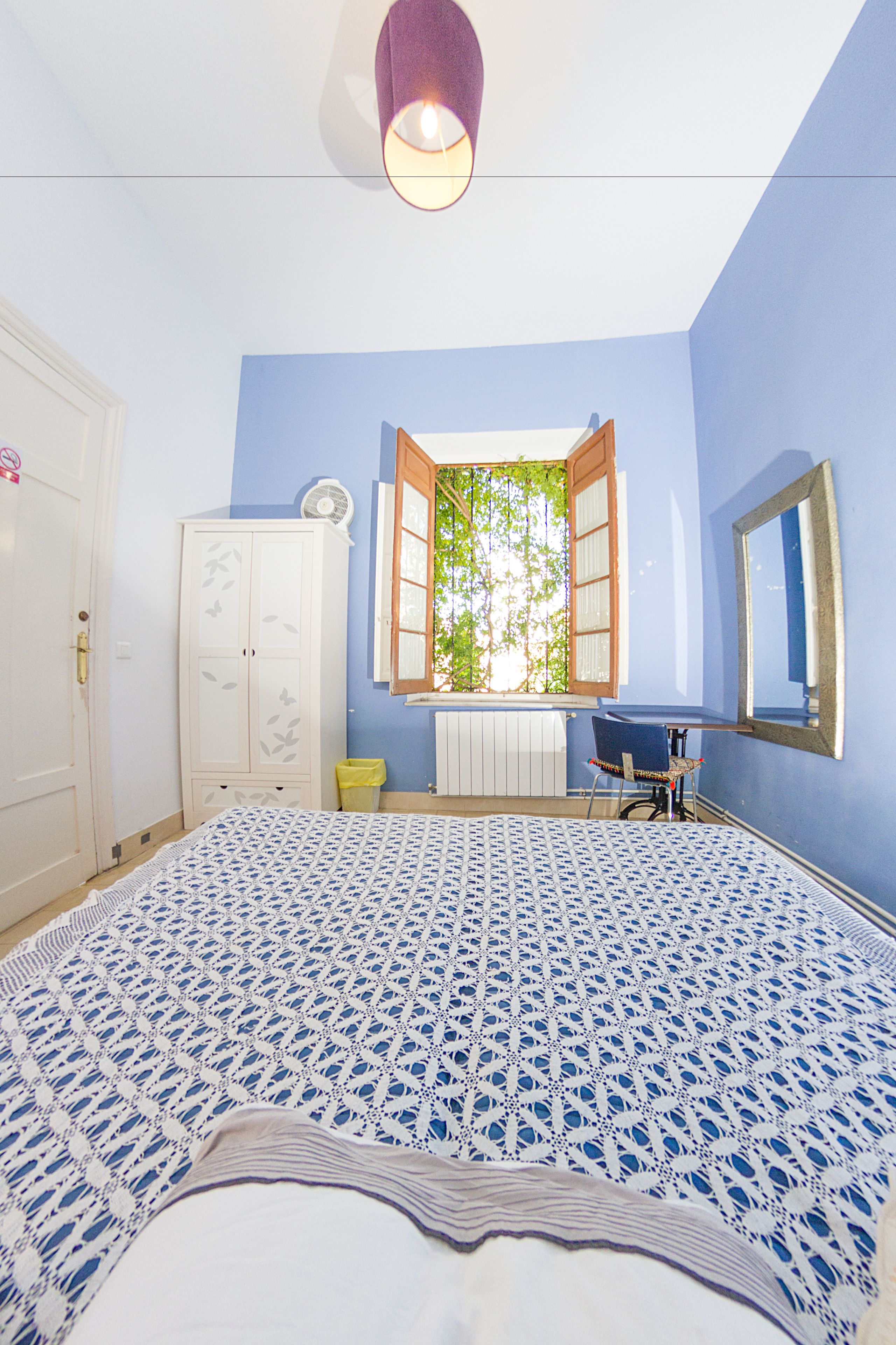 Un dormitorio con cama, armario, escritorio y ventana con contraventanas abiertas.