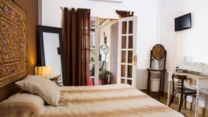 A hotel room with a bed, a desk, a chair, a television, and a door leading to a balcony. - Villa Alicia Guest House (Málaga)