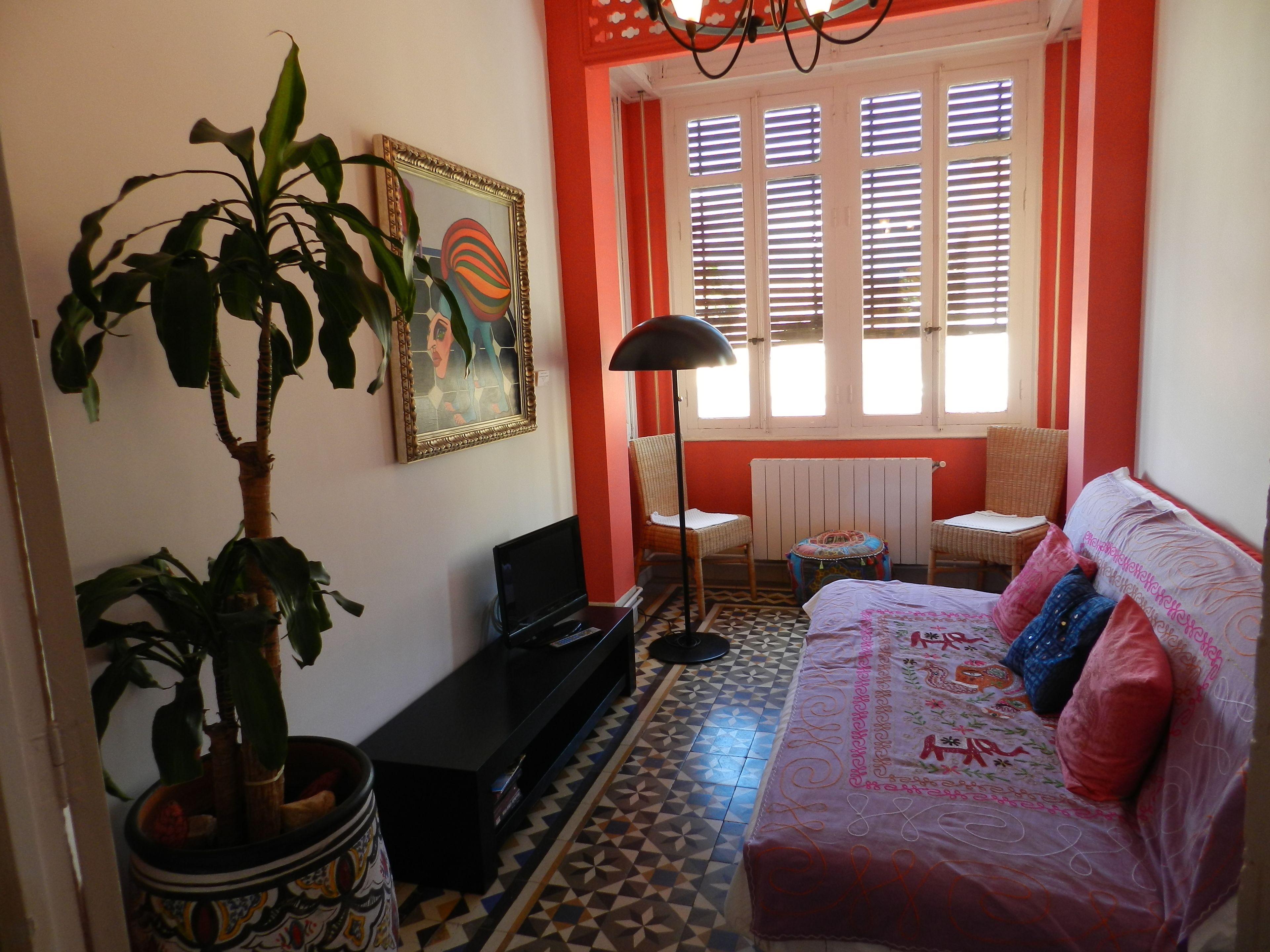 A living room with a sofa, a television, a potted plant, a painting, and a window with blinds.