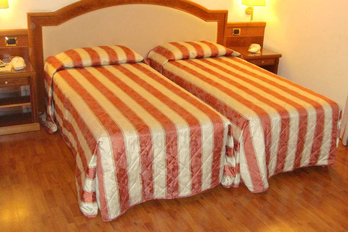 Una cama doble con ropa de cama a rayas, un cabecero de madera, mesitas de noche con lámparas y piso de madera.