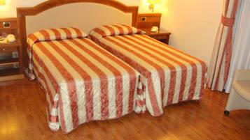 A double bed with striped bedding, a wooden headboard, bedside tables with lamps, and a wooden floor.