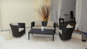 Een zithoek met een bank en twee fauteuils, een bijzettafeltje met een lantaarn, en een vaas met zonnebloemen.