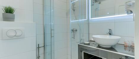 A modern bathroom with a glass-enclosed shower, a white sink, and a large mirror.