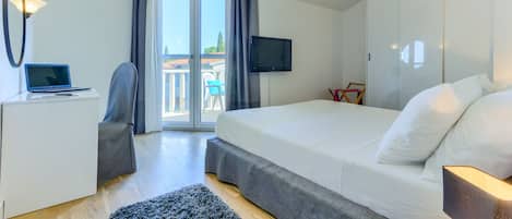 Habitación de hotel moderna con cama, escritorio con una laptop, televisión y balcón con vistas.