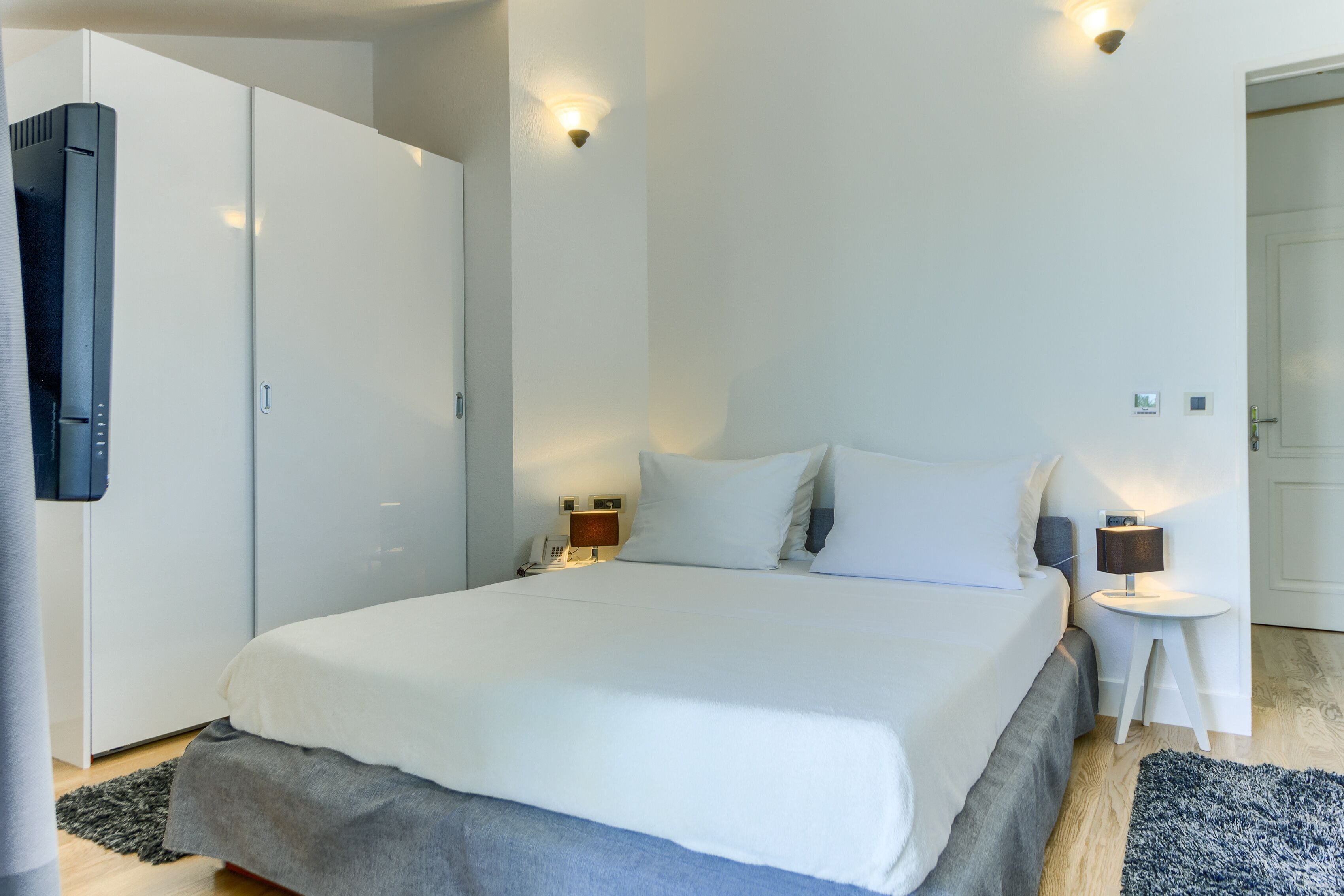 A modern bedroom with a large bed, bedside tables, a wardrobe, and a small side table with a lamp.