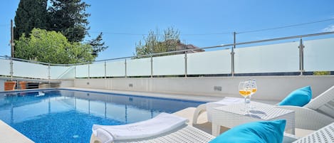 A swimming pool with white lounge chairs and blue cushions, surrounded by a white fence and trees.