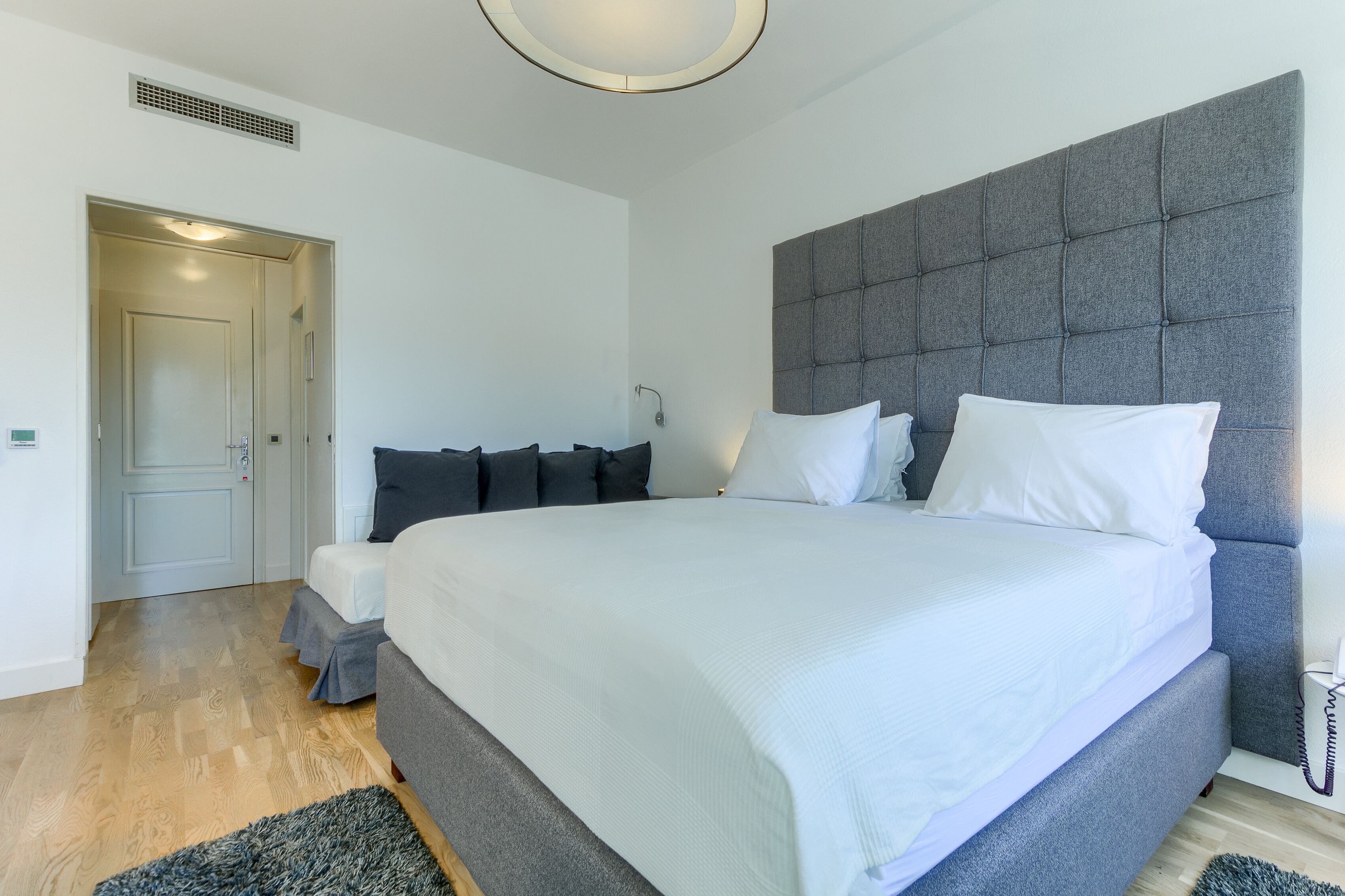 Un dormitorio moderno con una cama grande, cabecero tapizado color gris y suelo de madera.