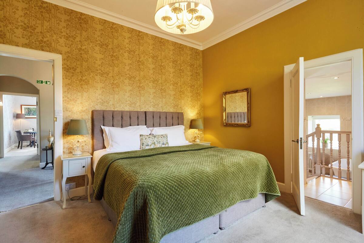 Habitación de hotel con cama, dos mesitas de noche, una araña y una puerta que da a un balcón.