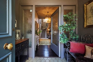 Un couloir avec un escalier, un plancher en bois, un banc avec un coussin rouge et une plante en pot.