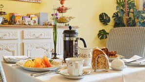Ein Frühstückstisch mit einer Kaffeekanne, Teller mit Speisen und einem Korbstuhl.