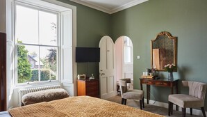 Ein Schlafzimmer mit großem Fenster, einem Bett mit strukturierter Decke, einem Schminktisch, einem Frisiertisch und einem Stuhl.