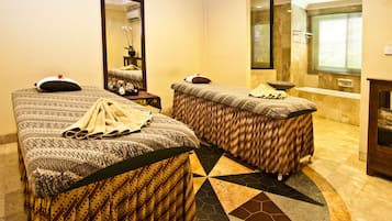 Two single beds with patterned bedspreads and matching pillows, a large mirror, and a small side table with a lamp.