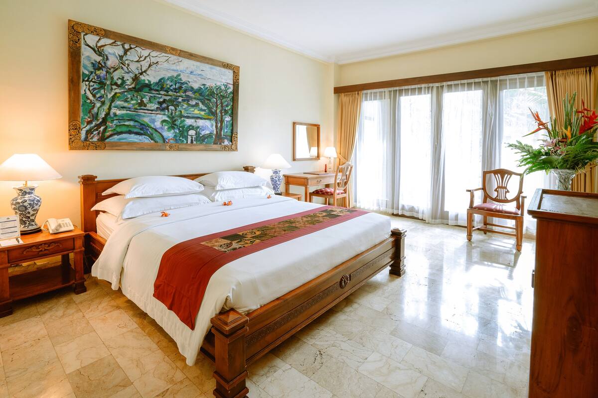 A spacious hotel room with a large bed, a desk, a chair, and a window with curtains.