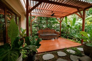 A wooden gazebo with a bench, surrounded by lush tropical plants and a stone pathway. - Hotel Kumala Pantai (Legian)