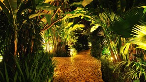 A stone pathway flanked by lush tropical foliage, leading through a garden area. - Hotel Kumala Pantai (Legian)