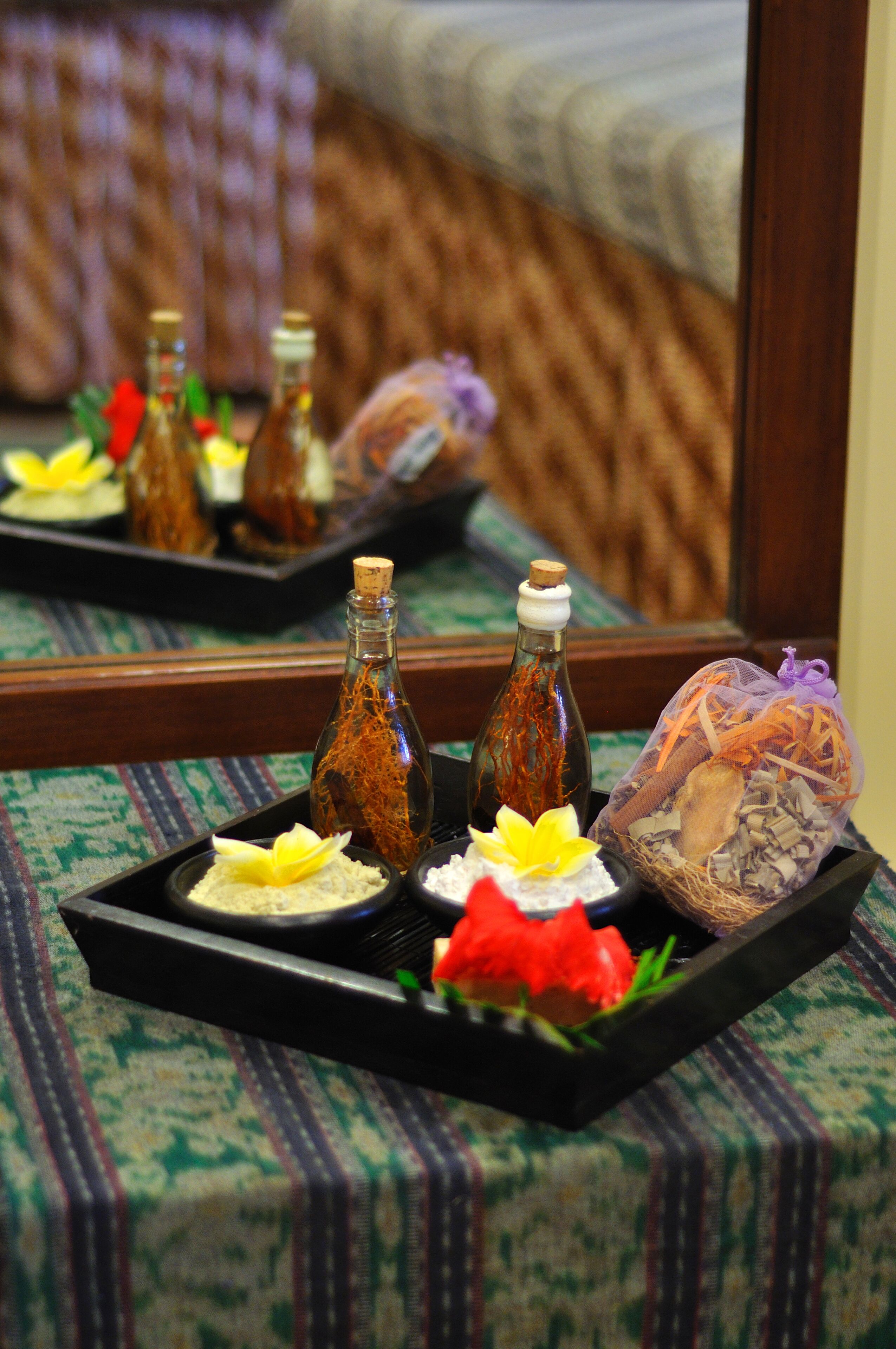 A tray with various items including bottles, a flower, and a decorative object on a patterned tablecloth.