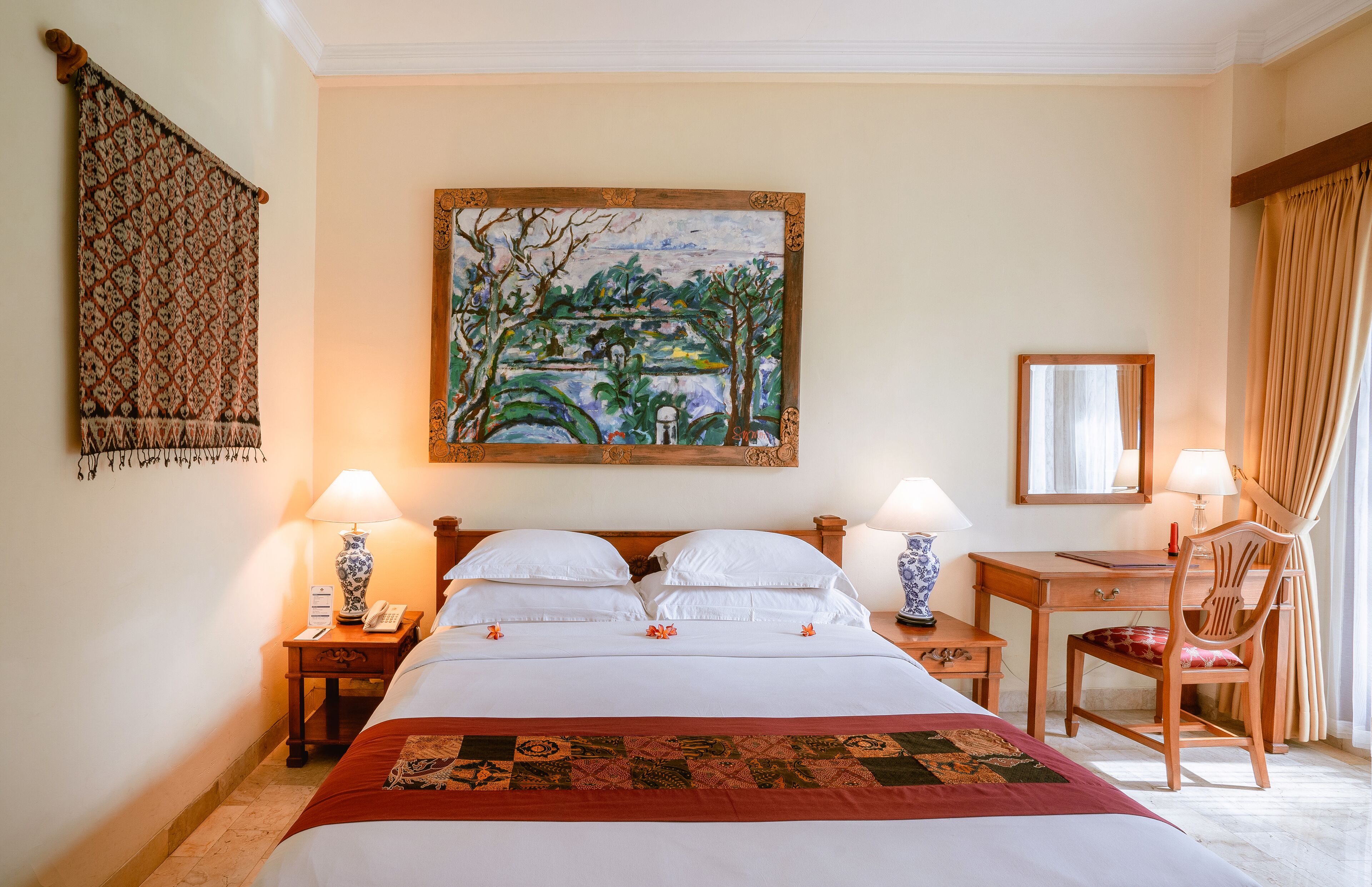 A hotel room with a large bed, two bedside tables with lamps, a desk with a chair, a painting on the wall, and a window with curtains.