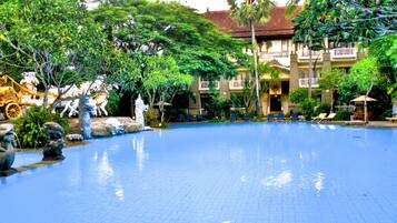 Relax by the serene pool surrounded by lush greenery and traditional architecture, featuring a spacious pool and comfortable lounge chairs.