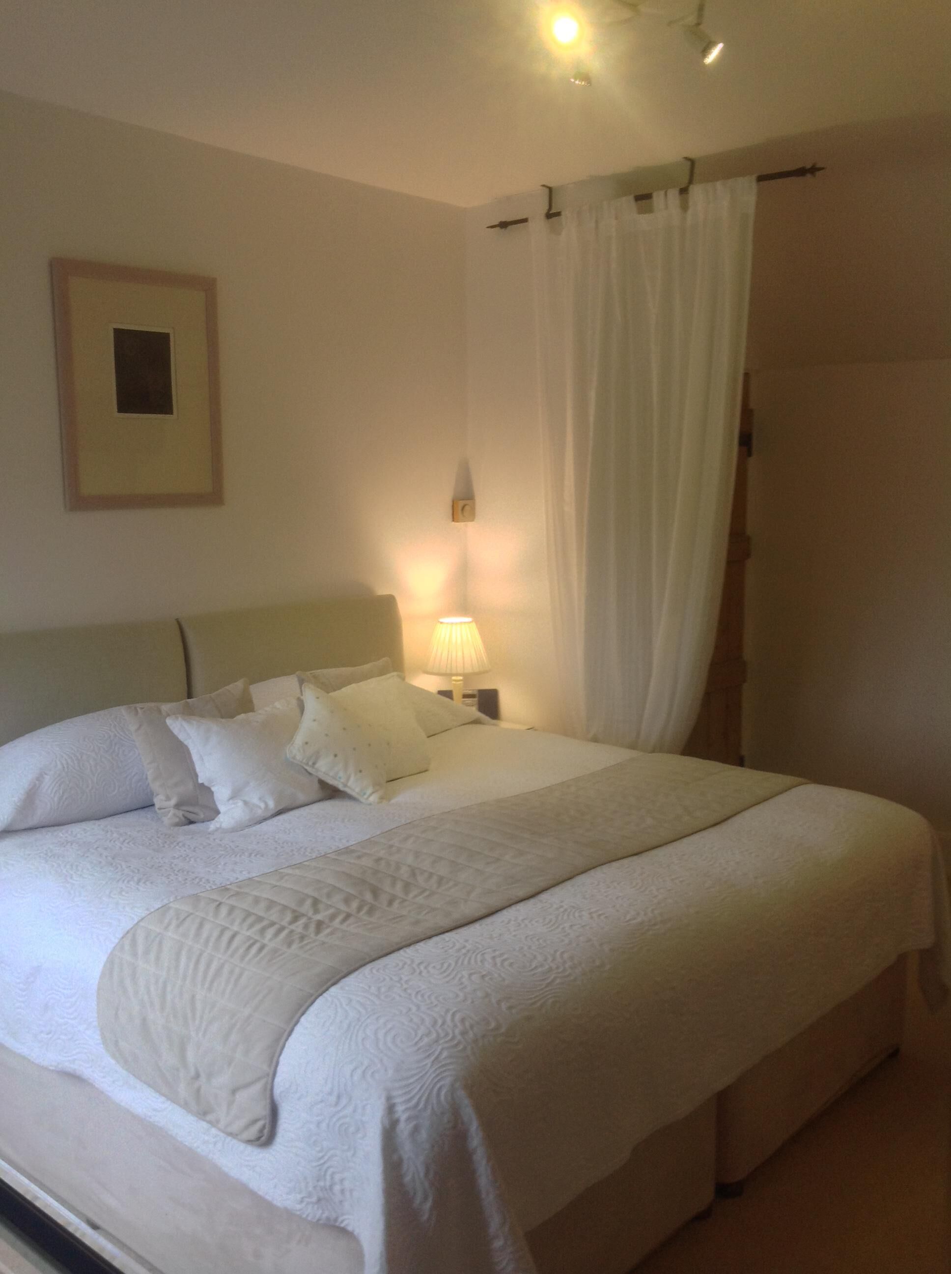 A neatly made bed with white linens and pillows, a bedside lamp, and a framed picture on the wall.