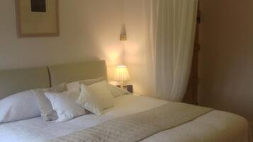 A neatly made bed with white linens and pillows, a bedside lamp, and a framed picture on the wall.