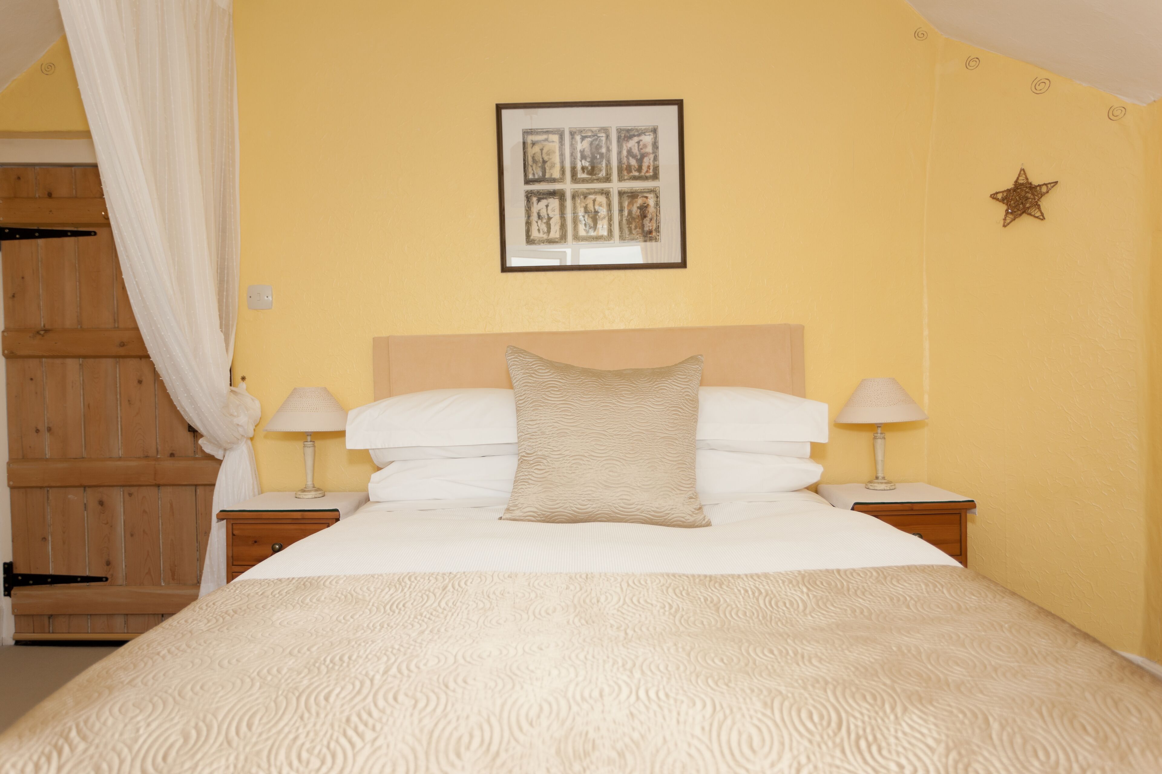 A bedroom with a bed, two bedside tables, a nightstand, a wooden wardrobe, and a wall-mounted picture.
