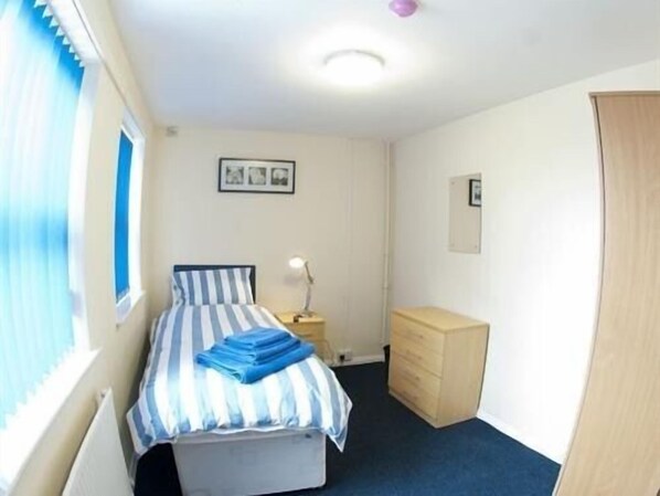 A bedroom with a bed, a dresser, a nightstand, and a window with blinds. - Liverpool Gateway Inn (Liverpool)
