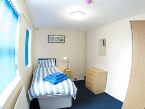 A bedroom with a bed, a dresser, a nightstand, and a window with blinds. - Liverpool Gateway Inn (Liverpool)