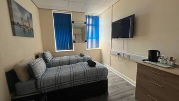 A bedroom with a bed, a TV, a dresser, and a window with curtains.