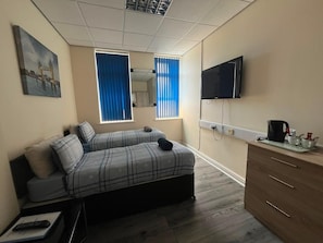 A bedroom with a bed, a TV, a dresser, and a window with curtains. - Liverpool Gateway Inn (Liverpool)