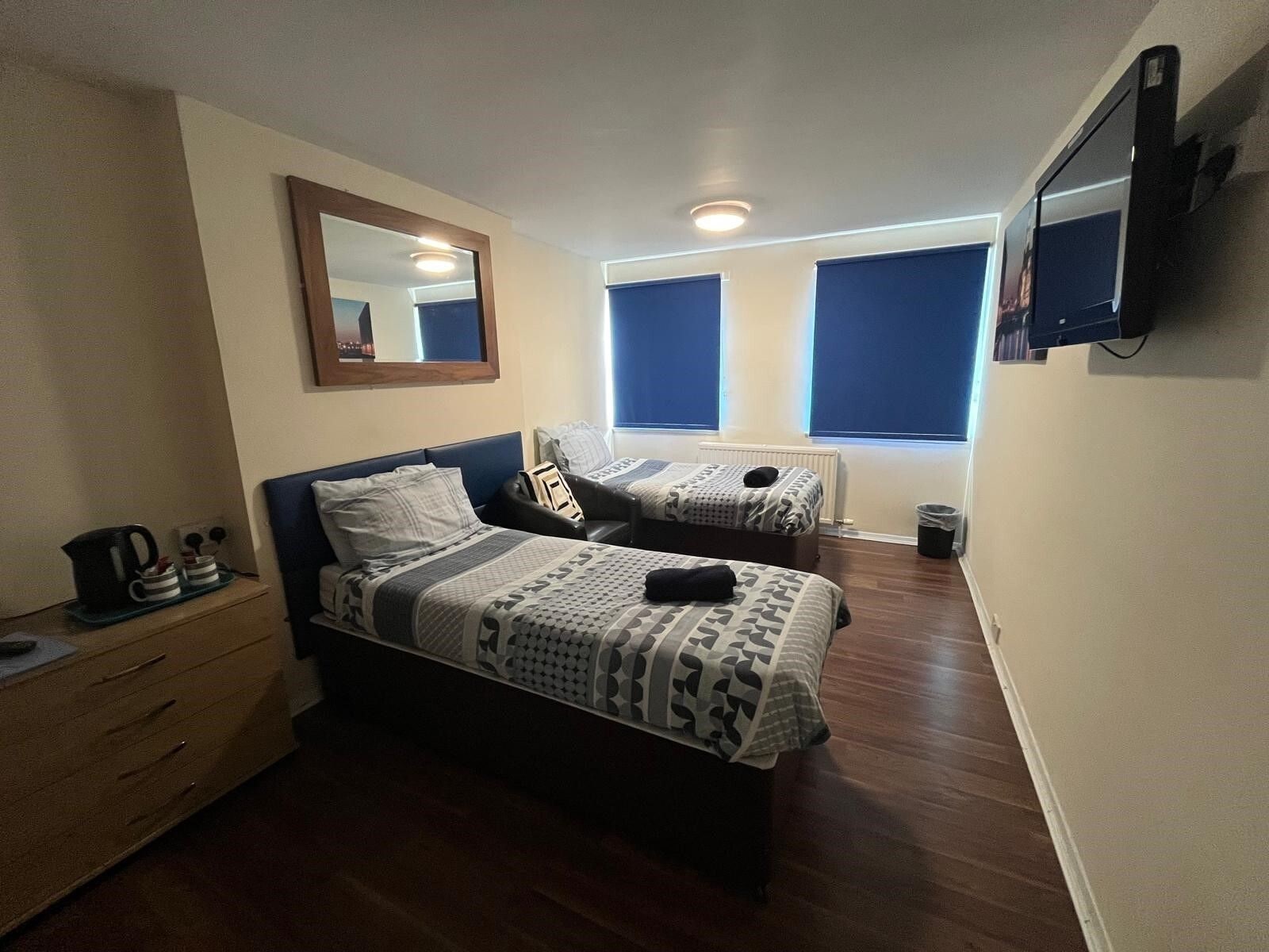 A hotel room with two beds, a dresser, a mirror, and a TV mounted on the wall.