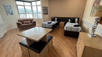 A modern room with a wooden floor, a sofa, two beds with pillows, a small table, and a lamp.