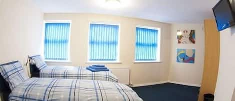 A bedroom with a bed, three windows, a wall-mounted TV, and artwork.