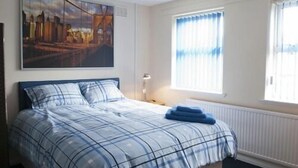 Een slaapkamer met een bed, een raam met gordijnen, een radiator en een aan de muur hangend schilderij.